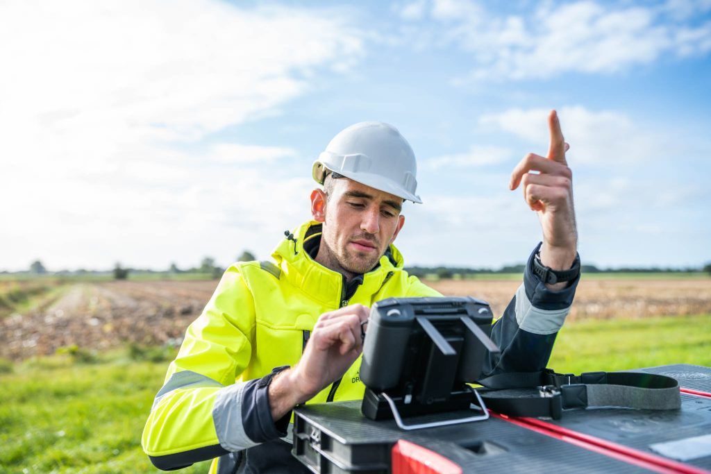 Man buiten met helm en gele reflecterende jas kijkt op scherm.