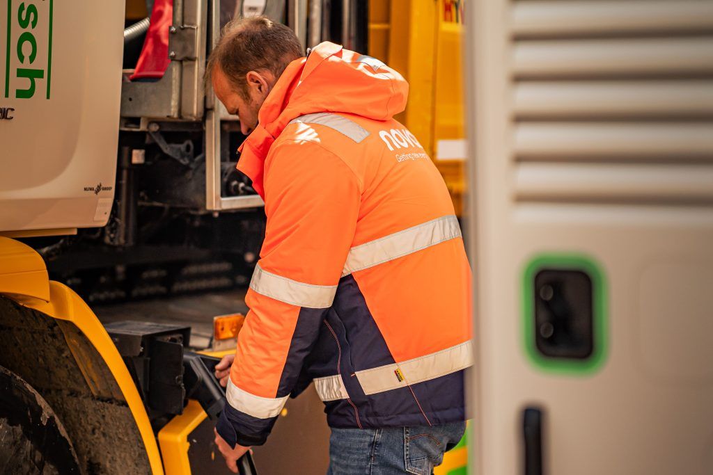 Man met oranje Novar jas laadt zijn elektrische vrachtwagen op.