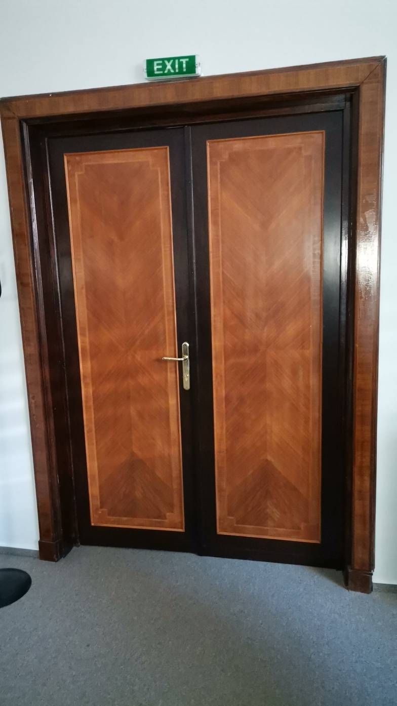 Ușă dublă din lemn cu un design geometric și mânere metalice, situată într-un interior.