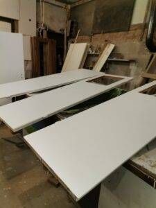 Trei uși albe netede așezate pe un suport în interiorul unui atelier de lucru.reconditionare usi furniruite