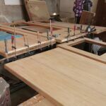 Uși din lemn așezate pe un banc de lucru, cu cleme de prindere aplicate pentru asamblare.