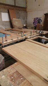 Uși din lemn așezate pe un banc de lucru, cu cleme de prindere aplicate pentru asamblare.