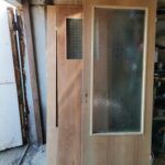 Uși din lemn cu un panou de sticlă decorativ, stând vertical în spațiu de lucru.