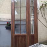 Ușă din lemn, acoperită cu folie, cu feronerie și geamuri laterale, stând în picioare.