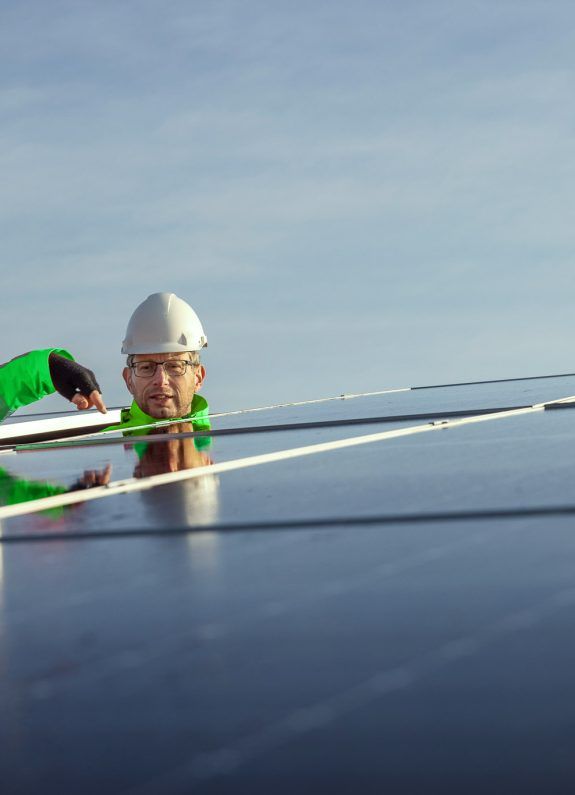 Twee experts met helmen inspecteren zonnepanelen onder een heldere lucht