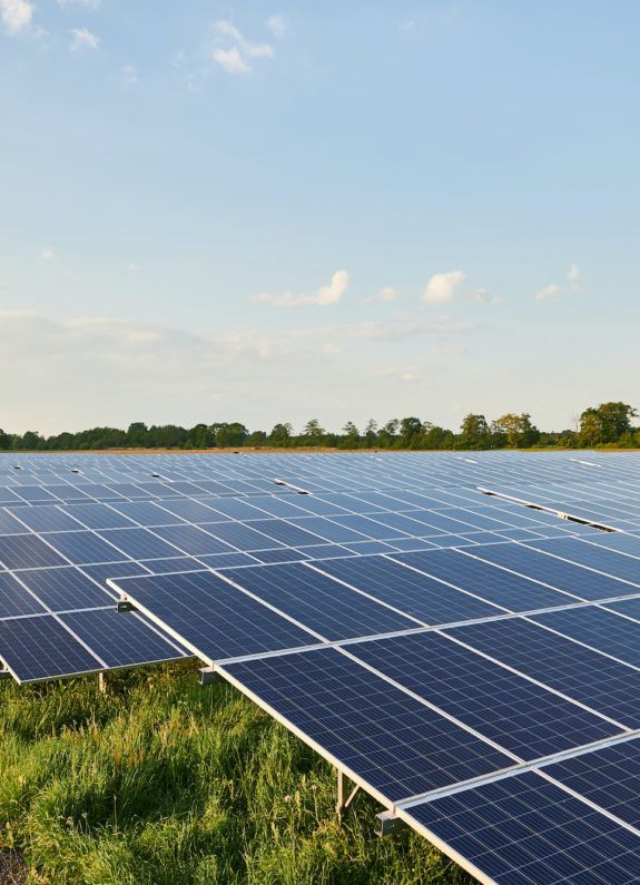 Grootschalig zonnepark met rijen zonnepanelen in een open landschap onder een blauwe lucht.