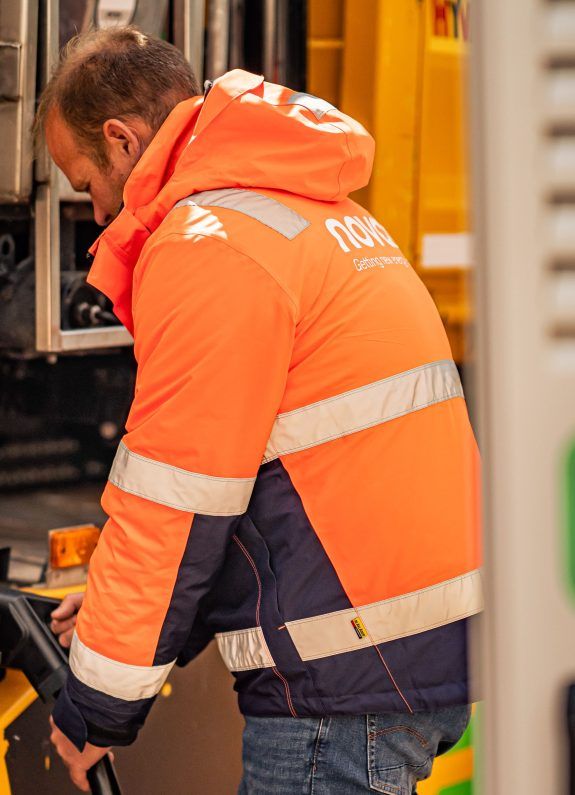 Man met oranje Novar jas laadt zijn elektrische vrachtwagen op.