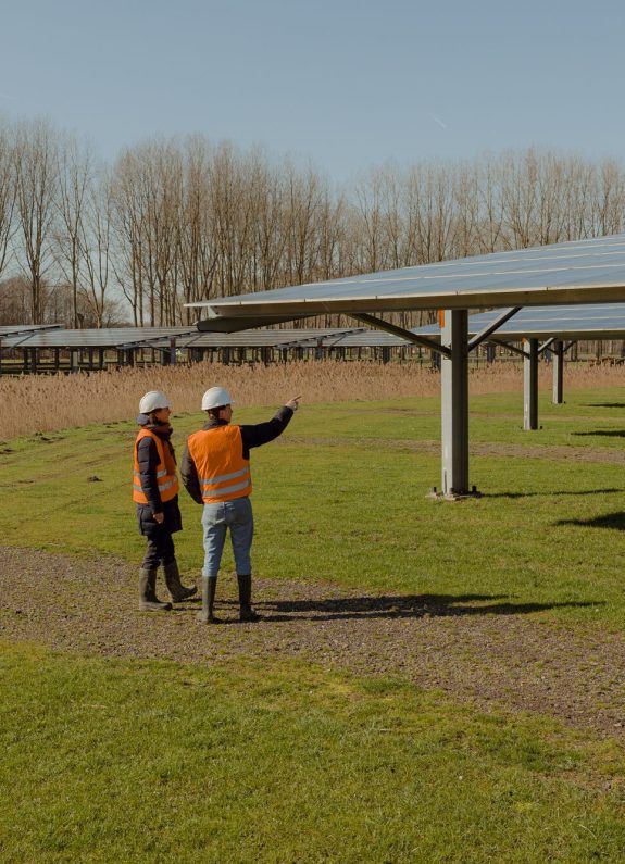 Twee medewerkers met veiligheidsvesten inspecteren een solar carport met zonnepanelen op een zonnige dag.