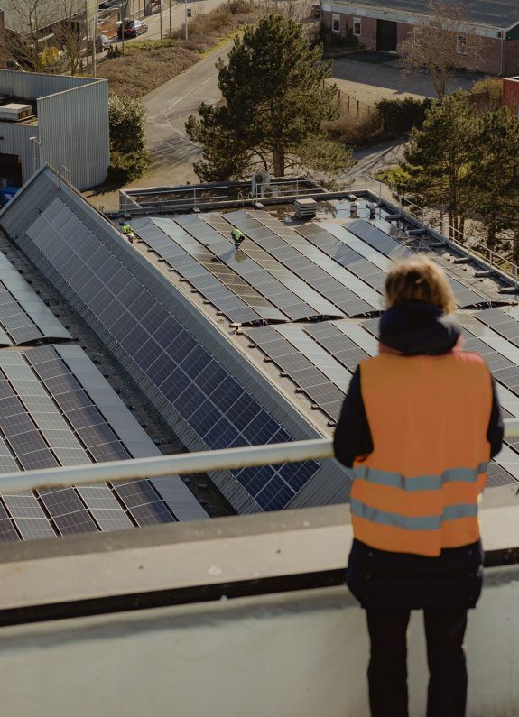Zonnepanelen op het dak van een bedrijfspand, met een medewerker die het zonnedak inspecteert.